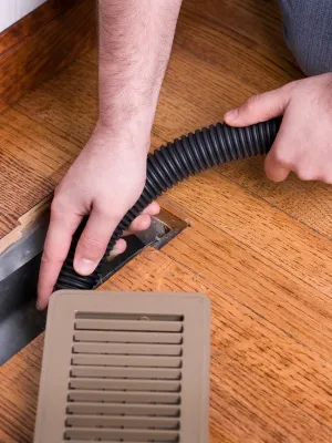 Homeowner cleaning dryer vent using vacuum hose to improve air flow and reduce fire risk in residential area