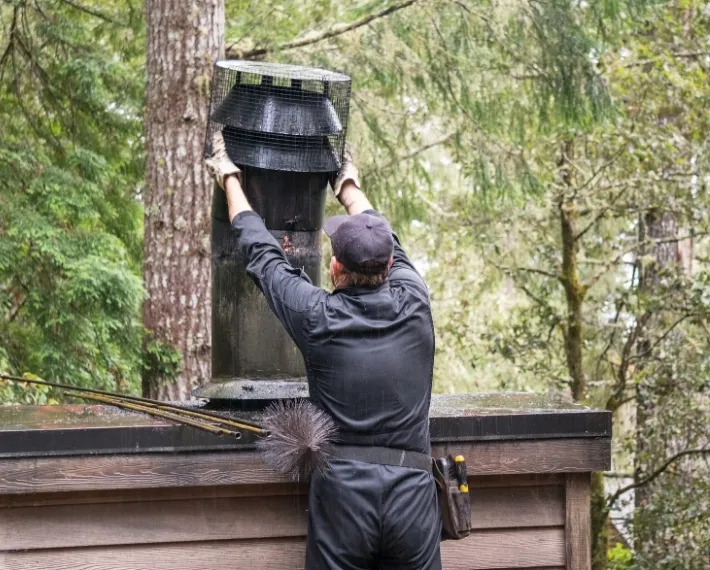 Chimney cleaning technician performs maintenance in New Jersey forested setting during daylight hours