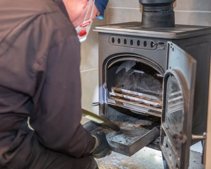 Professional chimney sweep service in New Jersey performing maintenance on a wood stove during the daytime